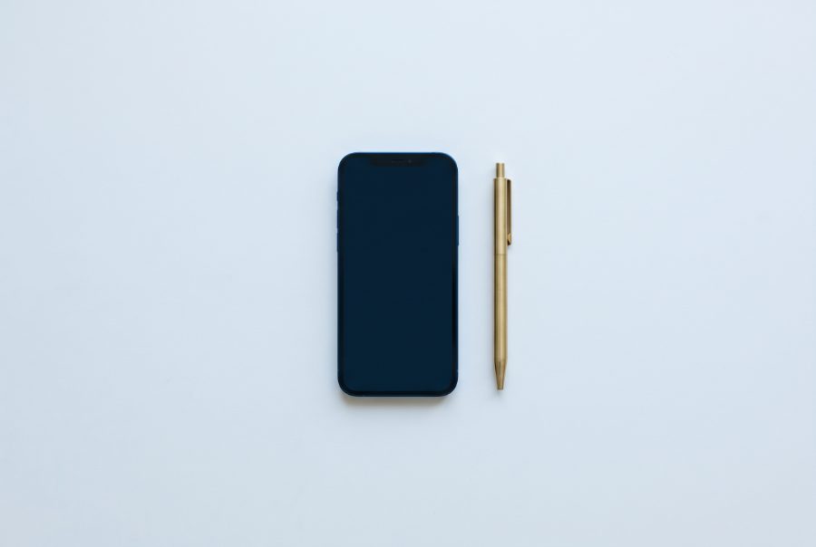 A phone lying face up on a desk beside a brass pen